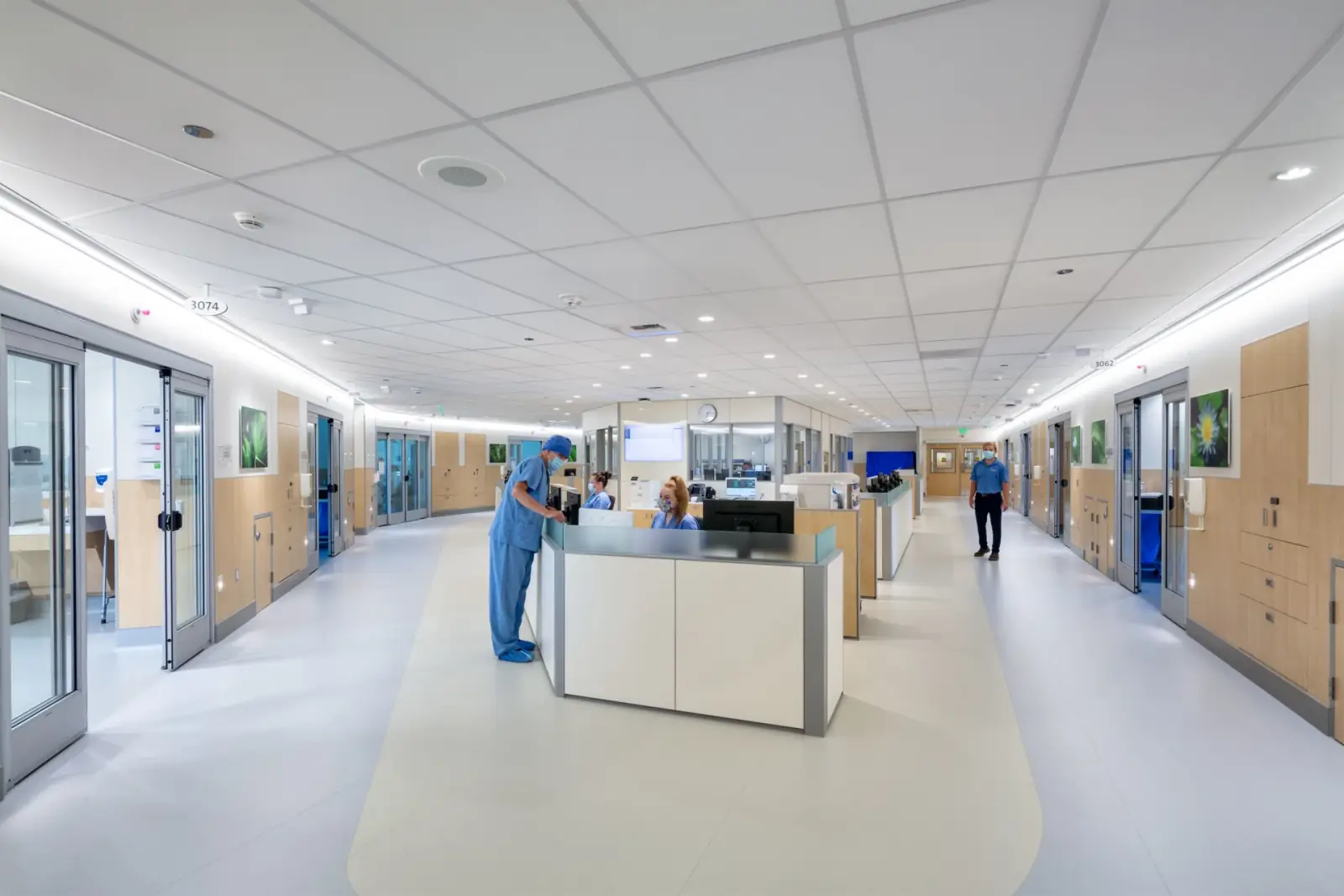 Bright hospital corridor with a central nurse station, modular wall panels and glass-fronted patient rooms