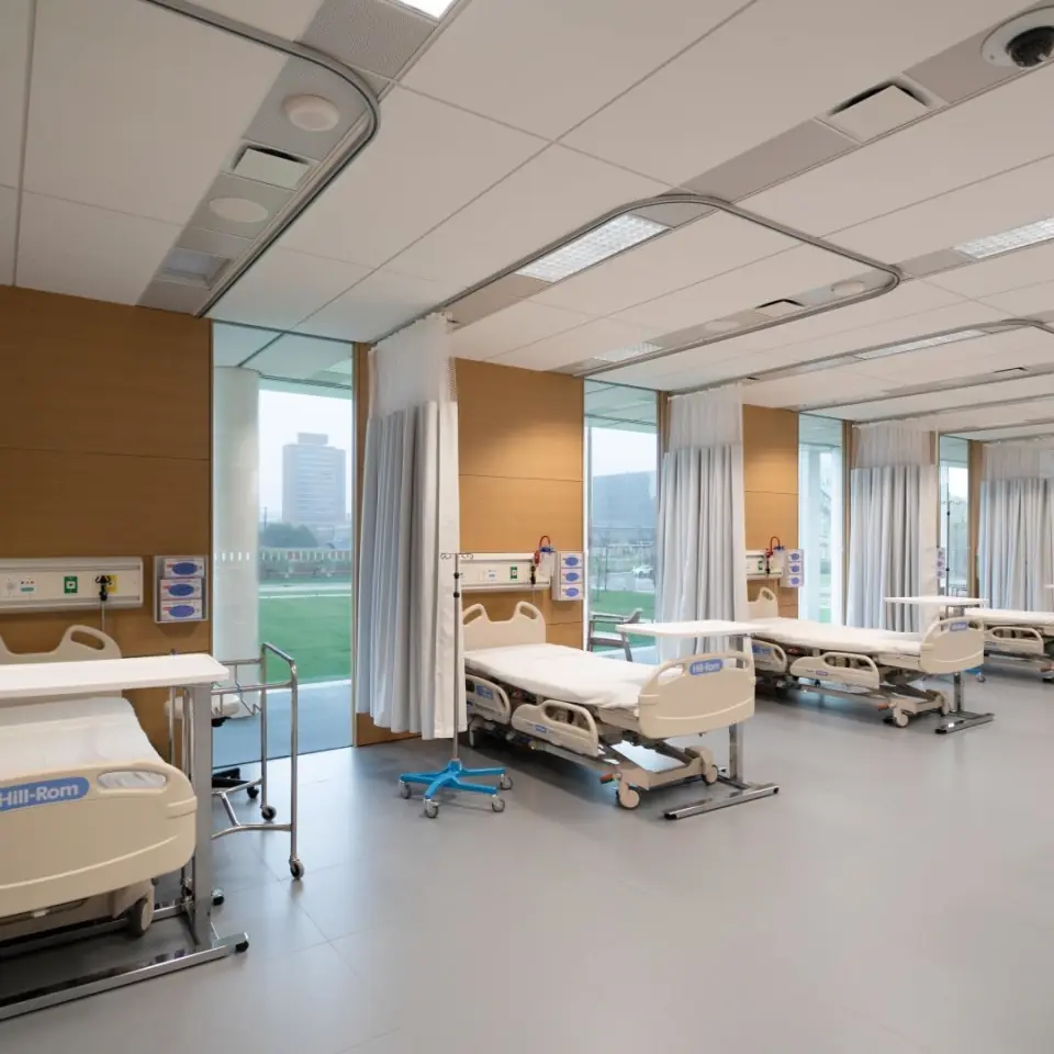 Multi-bed hospital ward with ceiling-track curtains and large windows
